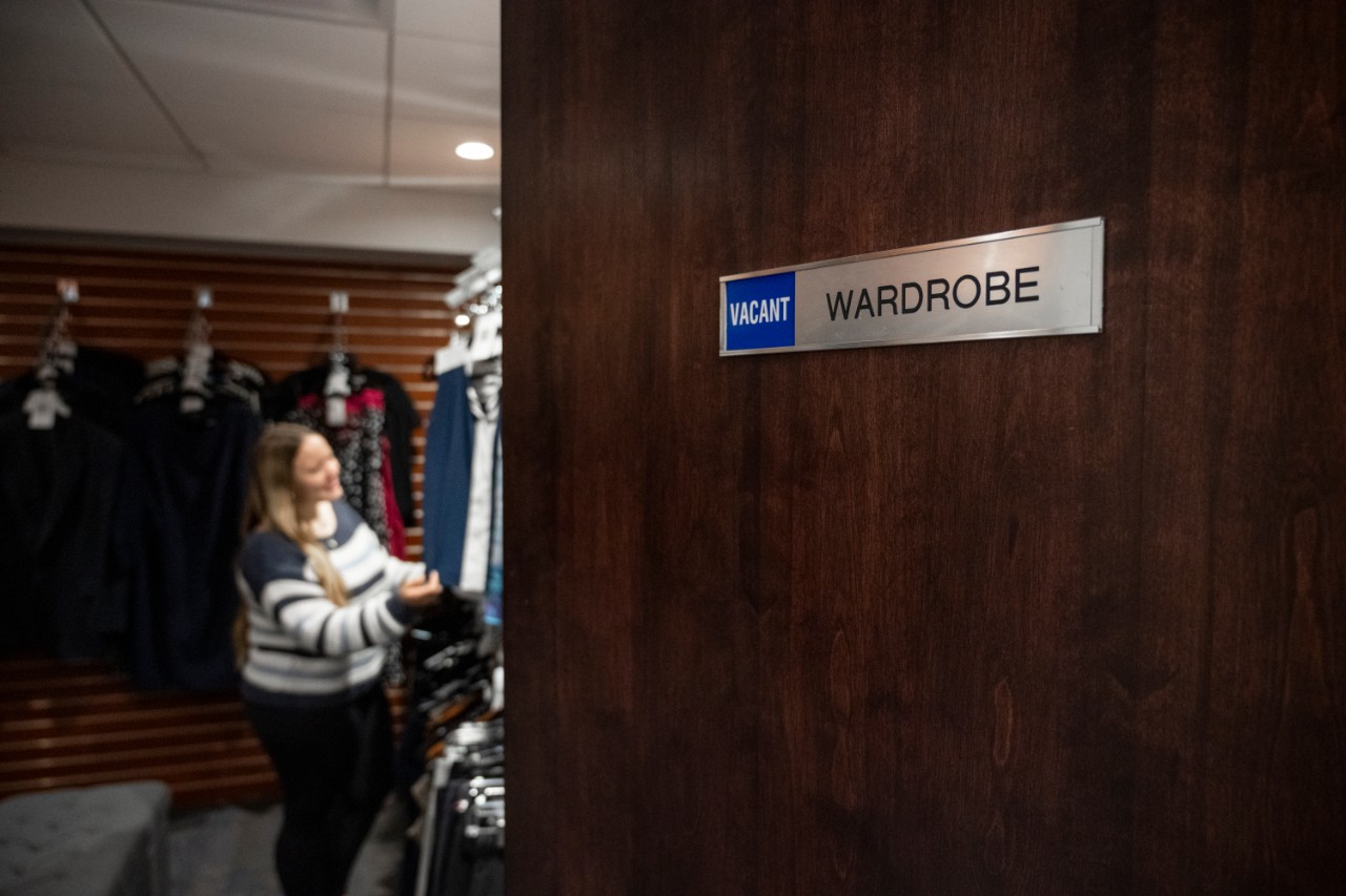 Student standing in the wardrobe looking at clothes with the door slightly open.