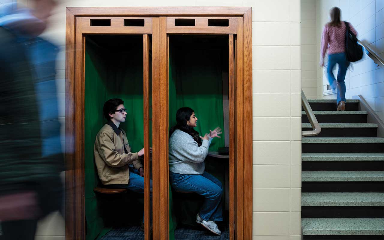 One male and one female student sit in separate Zoom booths in Bartley Hall.